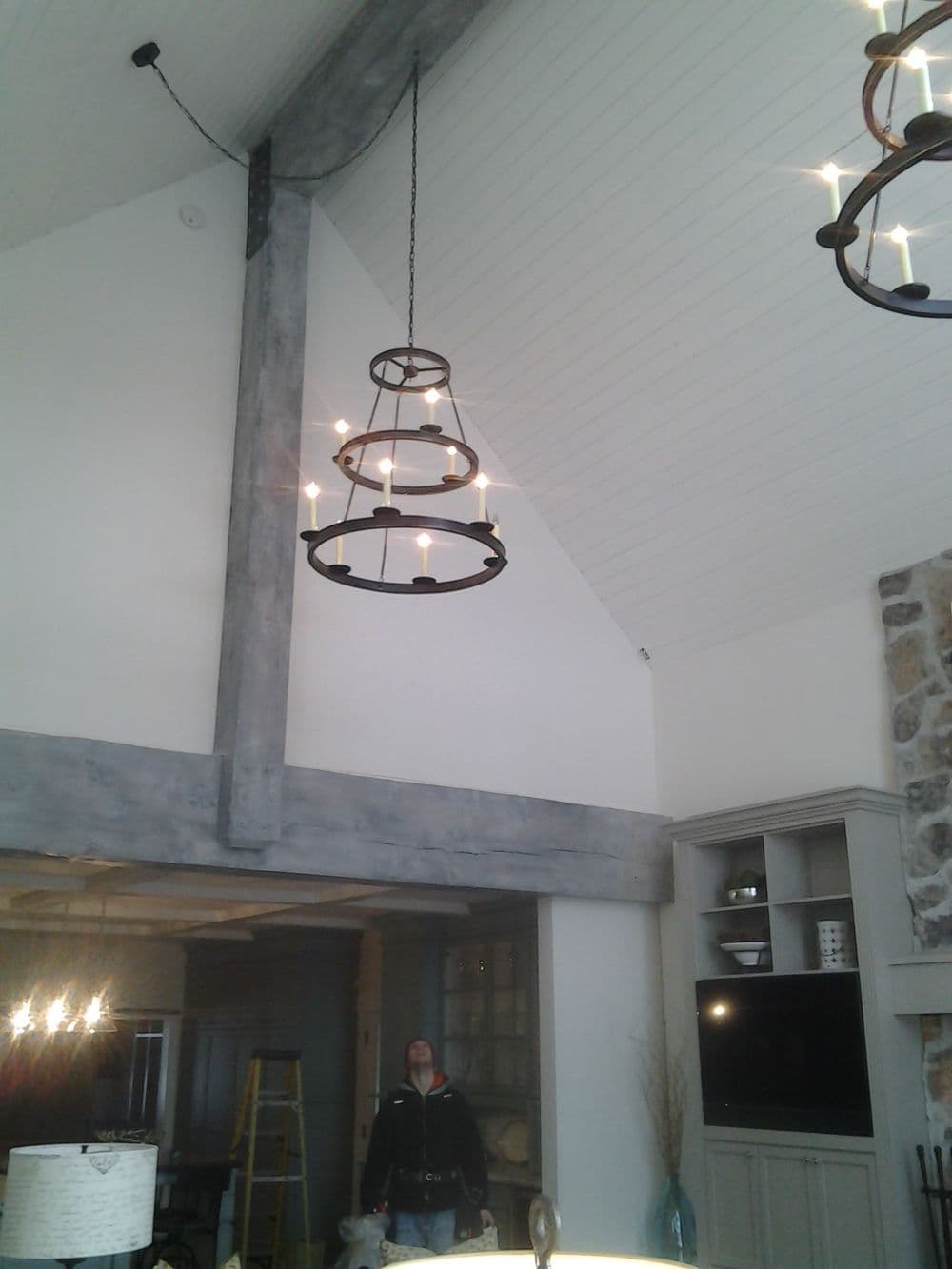 Modern industrial chandelier hanging in spacious living room with high ceiling beams.
