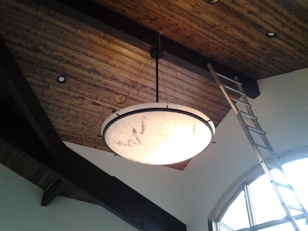 Modern round chandelier hanging from a wooden ceiling, with a ladder nearby for installation.