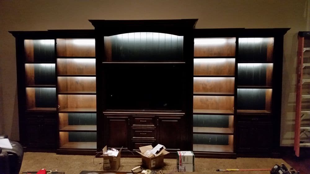 Large wooden entertainment center with built-in shelves and bottom storage, illuminated with lights.