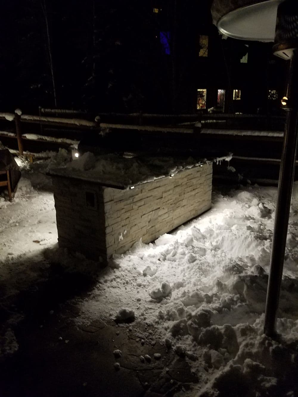 Snow-covered patio with a stone heater illuminated at night.