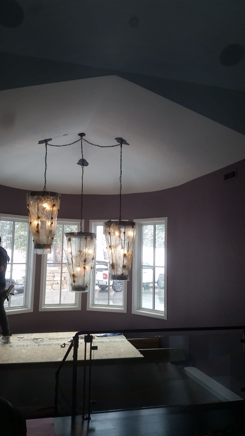 Modern chandelier lights hang over a stairwell with large windows. Stylish interior design.
