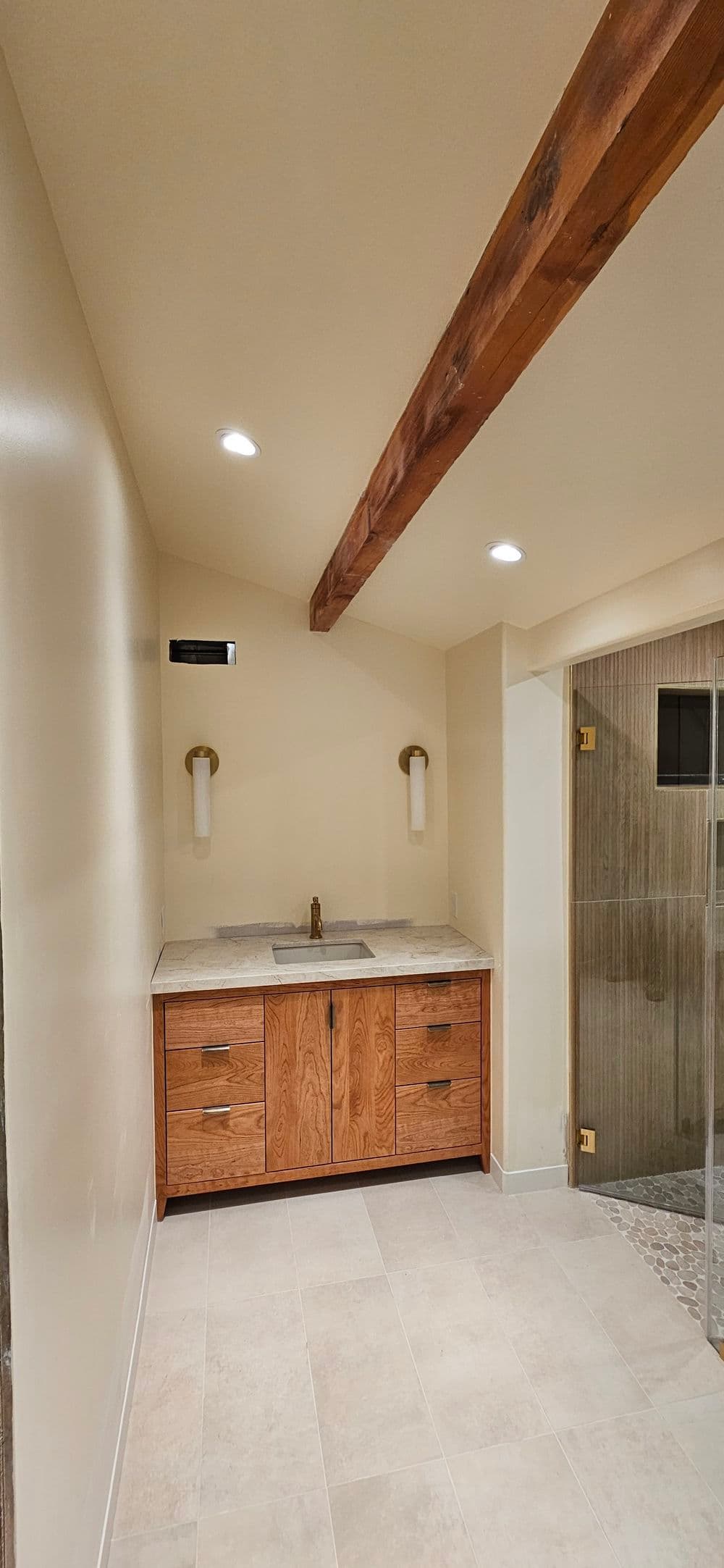 Modern bathroom interior with wooden vanity, stone countertop, and shower area featuring glass doors.