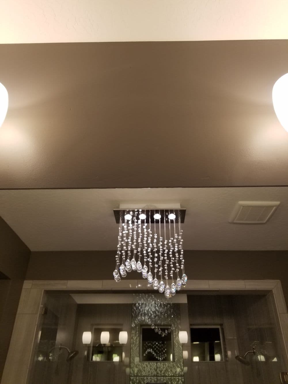 Modern bathroom with elegant crystal chandelier and stylish wall sconces.