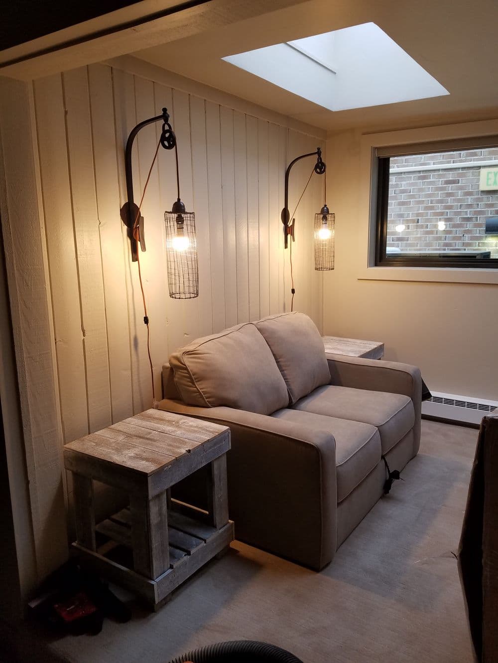 Cozy seating area with a gray loveseat, wooden side tables, and stylish wall lights.