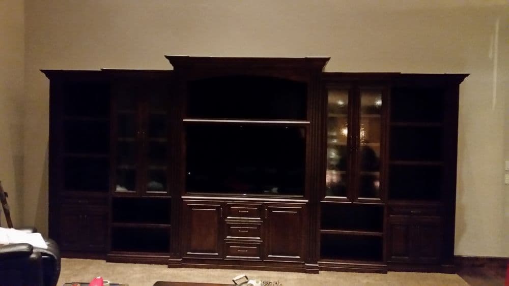 Dark wood entertainment center with glass shelves and built-in TV space in a living room.