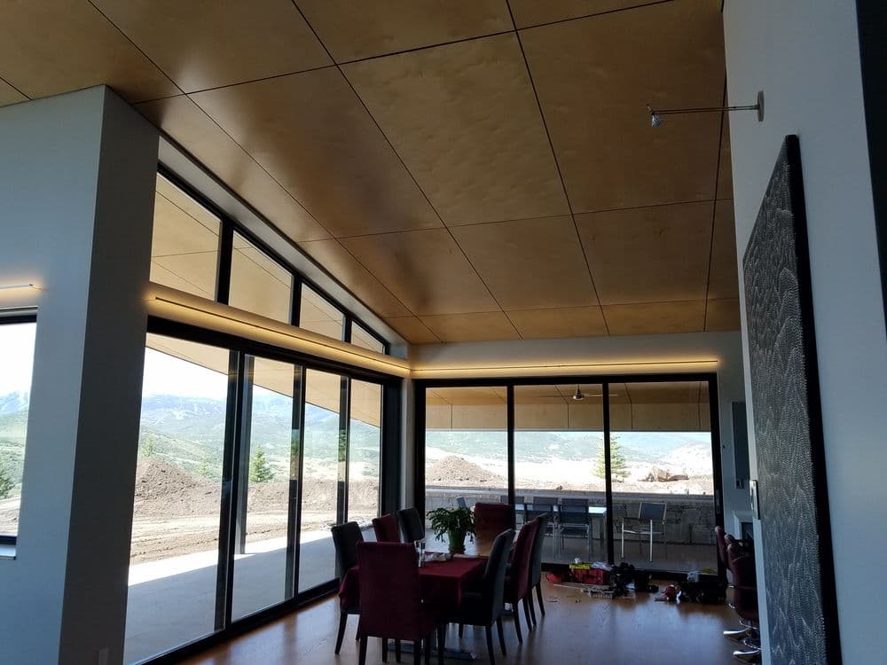 Modern dining area with large windows, wooden ceiling, and mountain view.