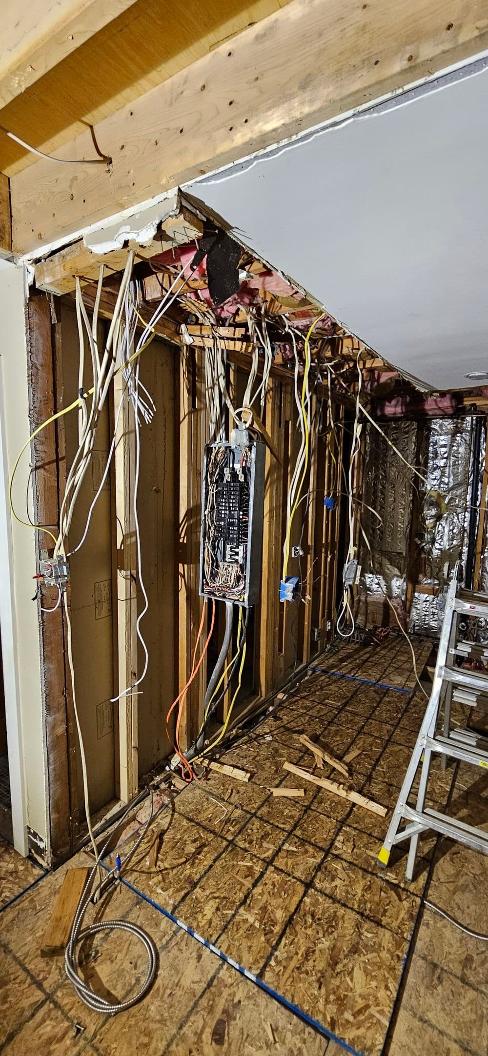 Exposed electrical wiring and open walls in a home renovation project. Construction tools visible.