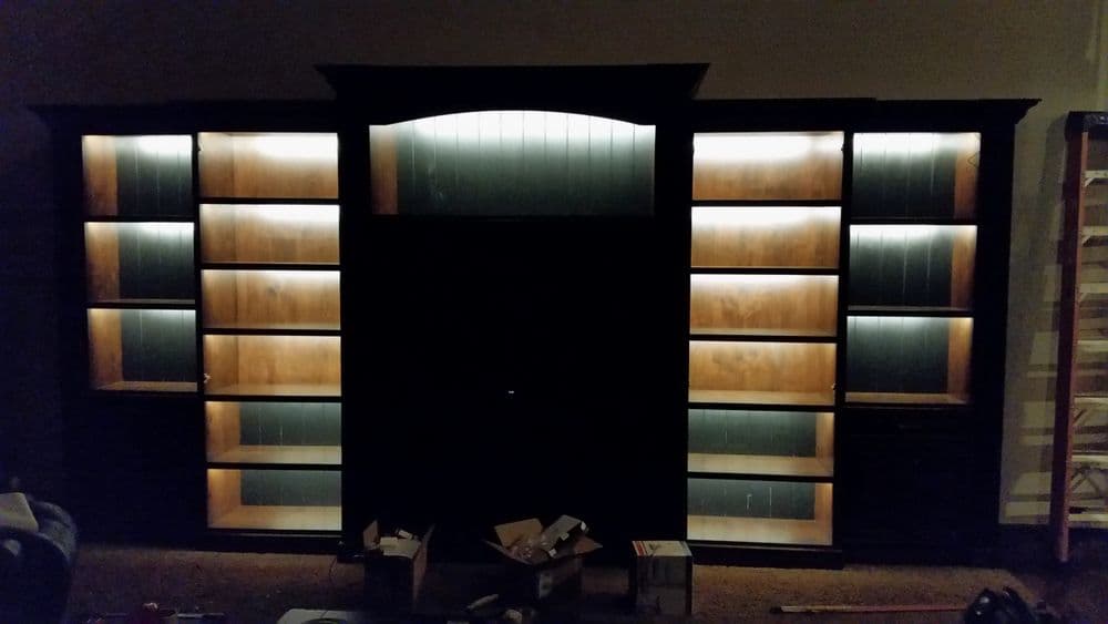 Dark wooden bookshelf with illuminated shelves and open center, surrounded by boxes.