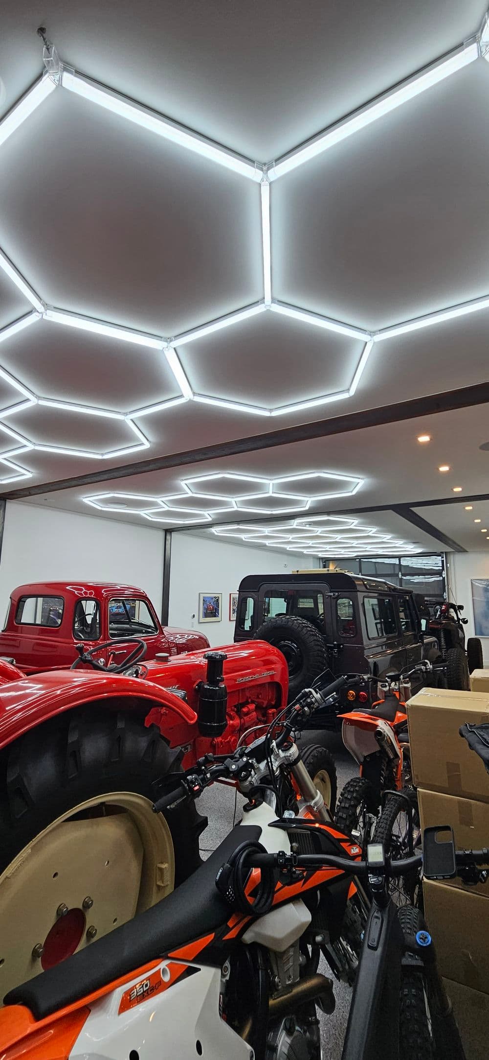 Modern garage showcasing vintage cars, motorcycles, and a unique hexagonal LED ceiling design.