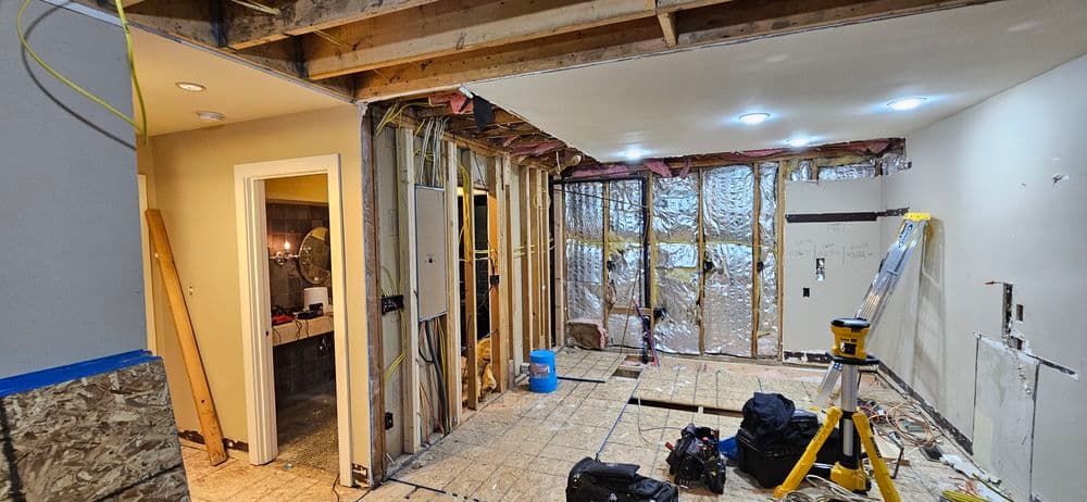 Home renovation progress showing exposed walls, insulation, and tools in an unfinished space.