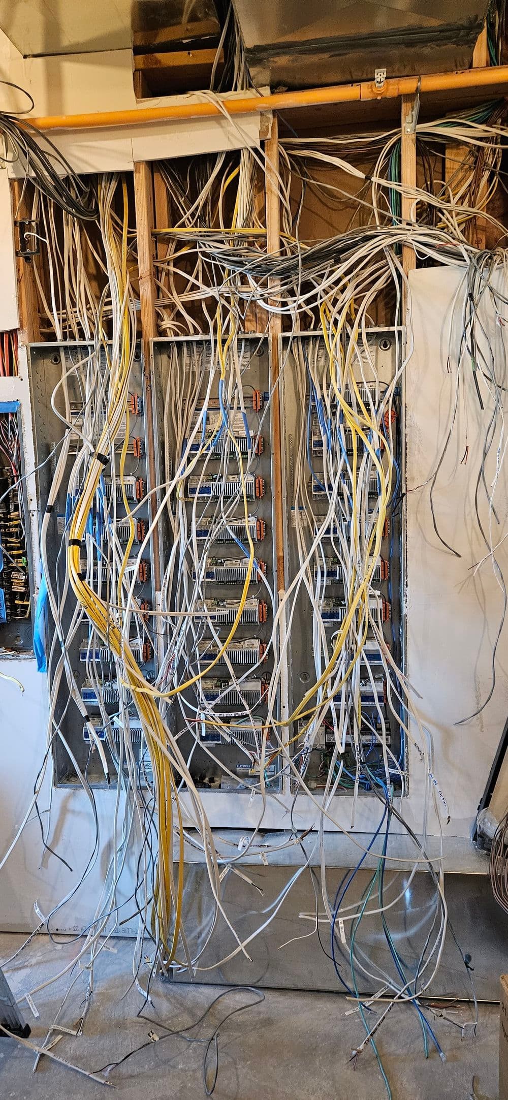 Messy network wiring and electrical panel in a home, showcasing tangled cables and connections.