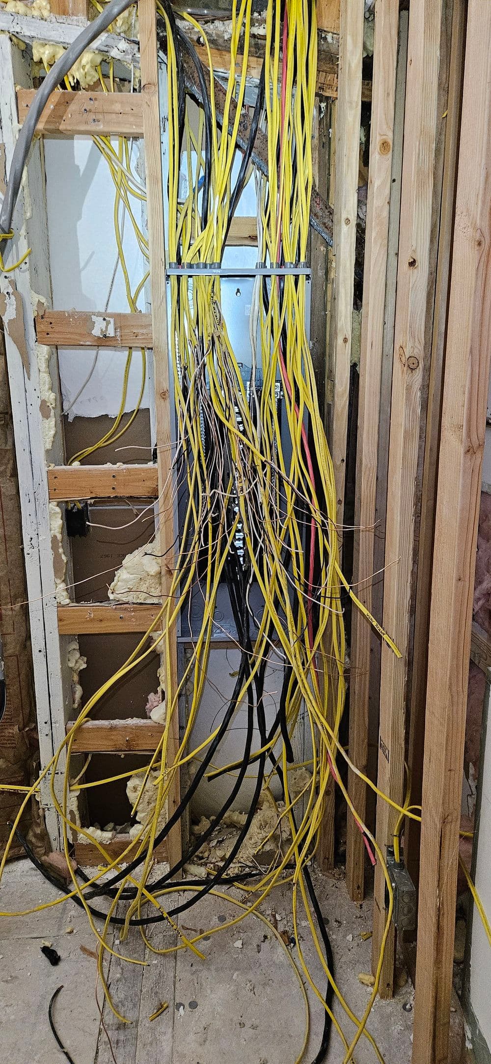 Disorganized electrical wiring in a partially constructed wall, showcasing yellow and black cables.