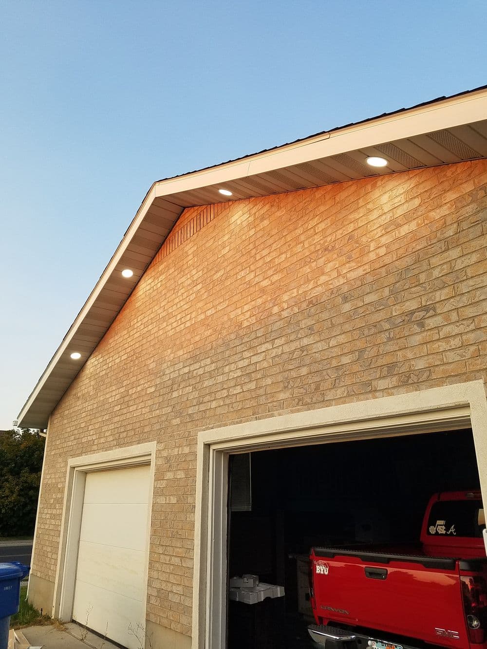 Exterior view of a garage with recessed lighting under the eaves at sunset.