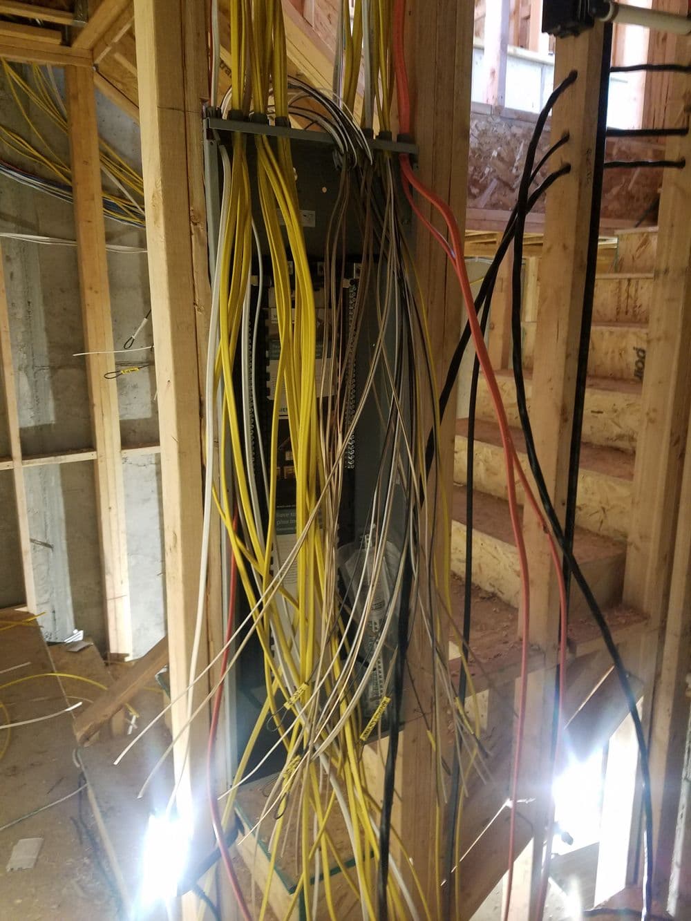 Electrical panel with numerous wires in a partially constructed building interior.