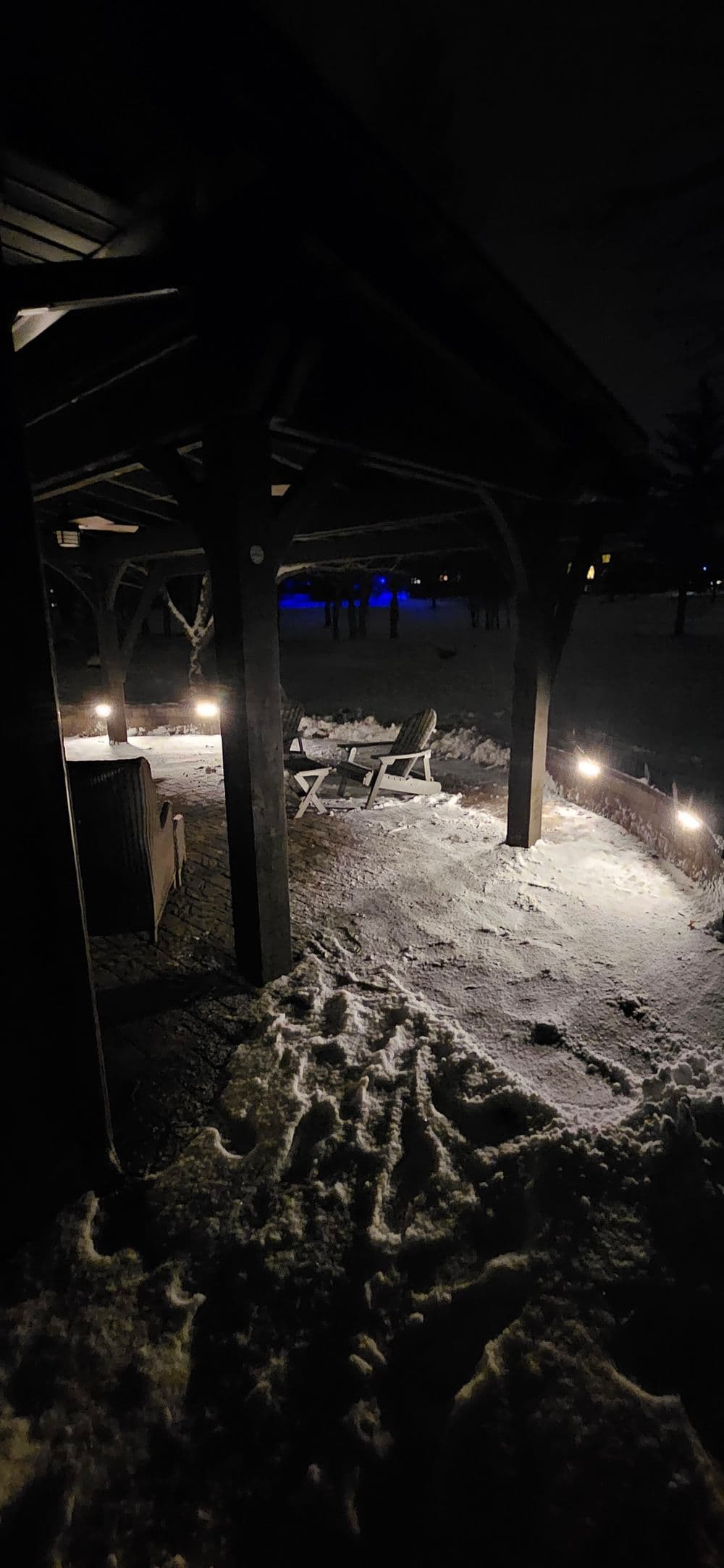snowy outdoor patio at night with illuminated pathways and lounge chairs under a covered structure