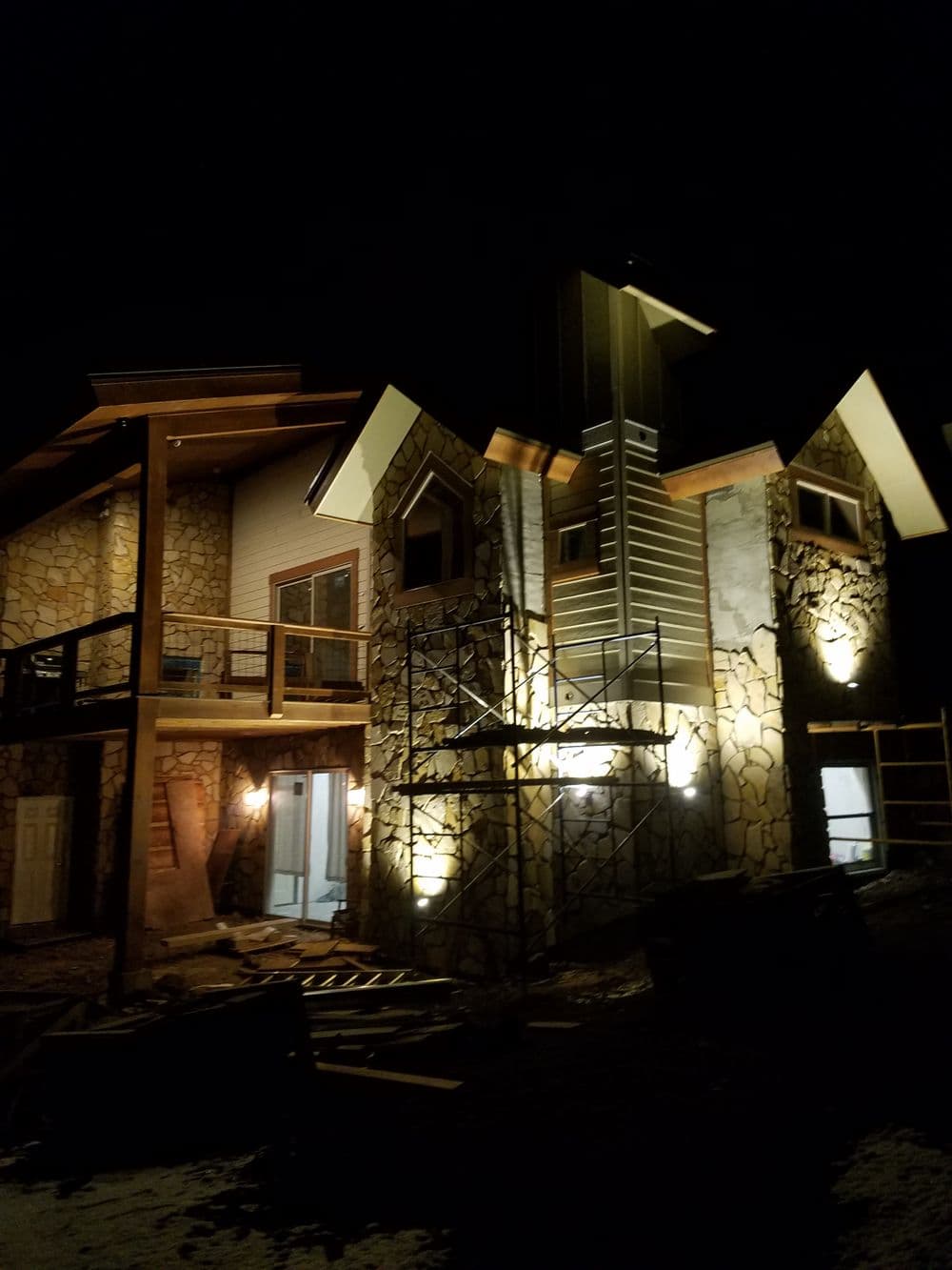 Modern stone house at night with decorative lighting and scaffolding, showcasing unique architecture.
