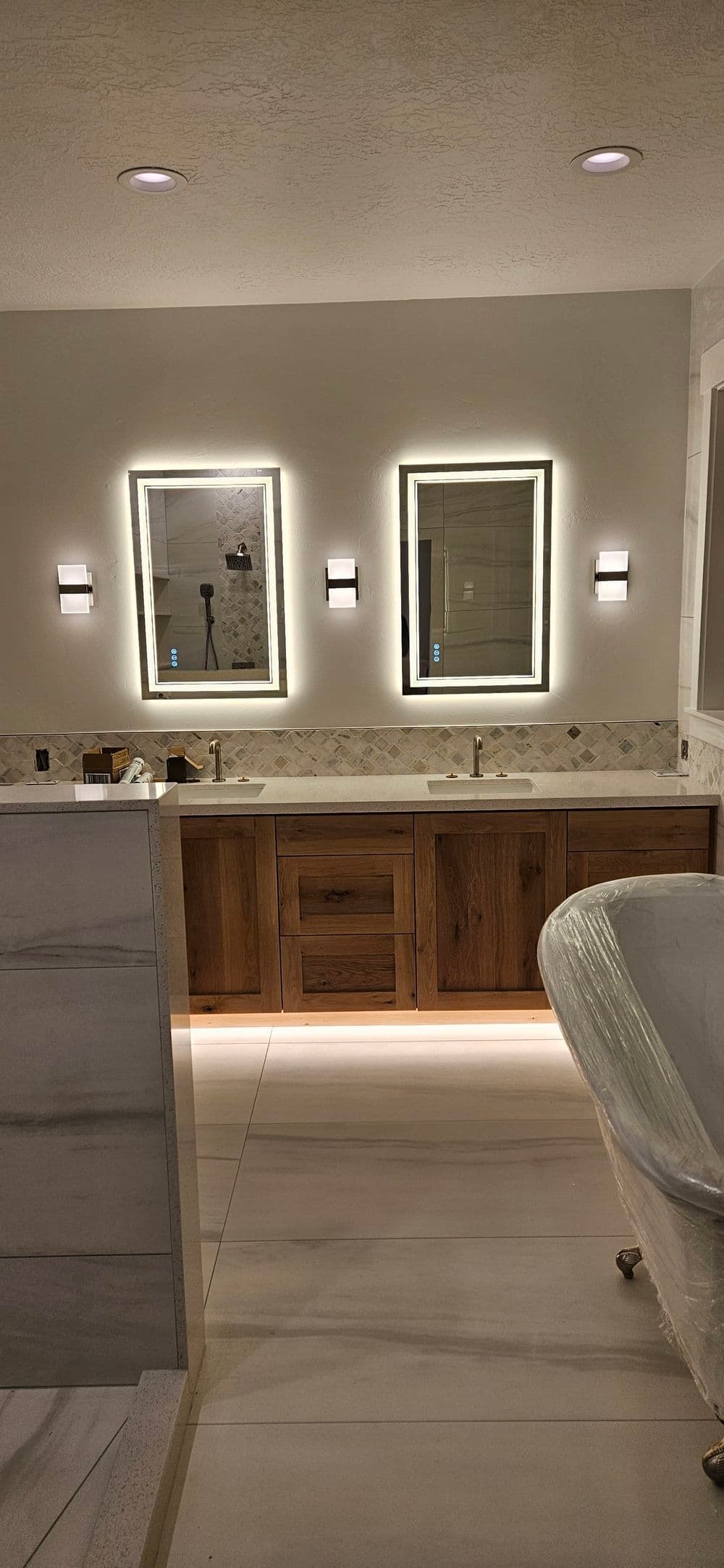 Modern bathroom with dual mirrors, stylish lighting, wooden vanity, and elegant tub.