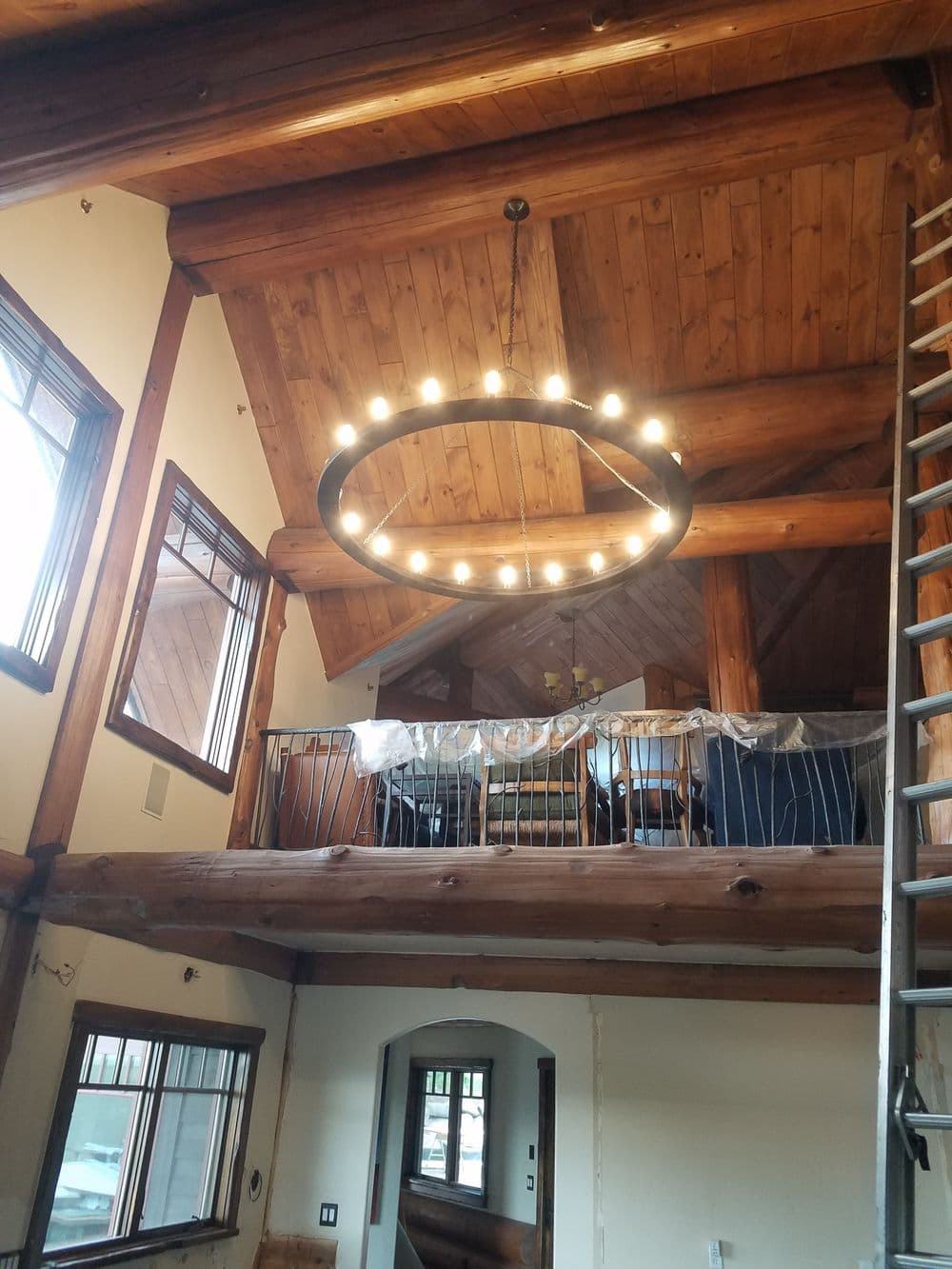 Modern circular chandelier in a rustic wooden interior with high ceilings and exposed beams.