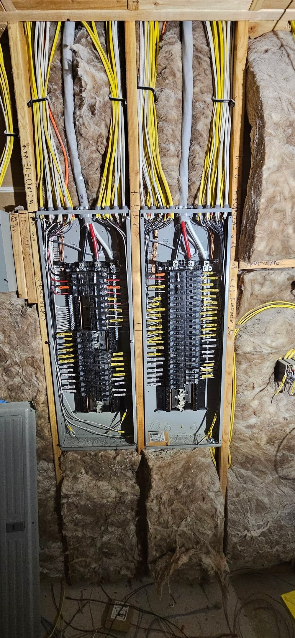 Electrical panels with labeled circuit breakers and wiring in a construction setting.