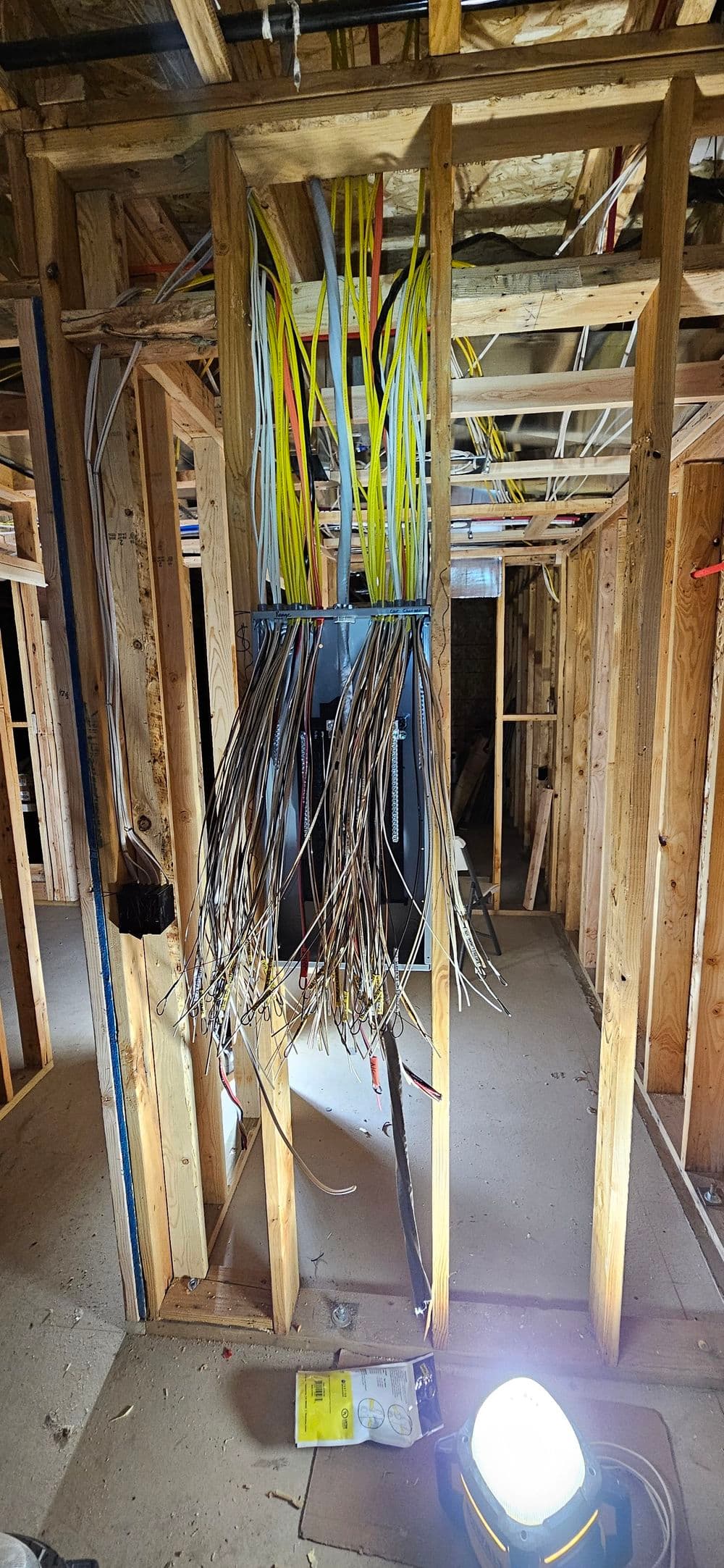 Electrical panel surrounded by exposed wiring in a construction interior. Bright work light visible.