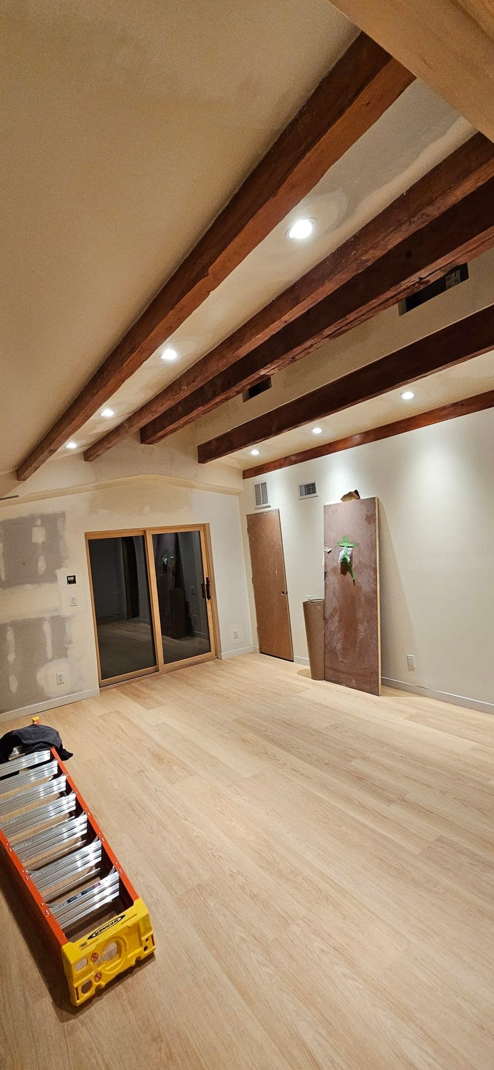 Renovated interior room with wooden beams, recessed lighting, and a ladder on the floor.