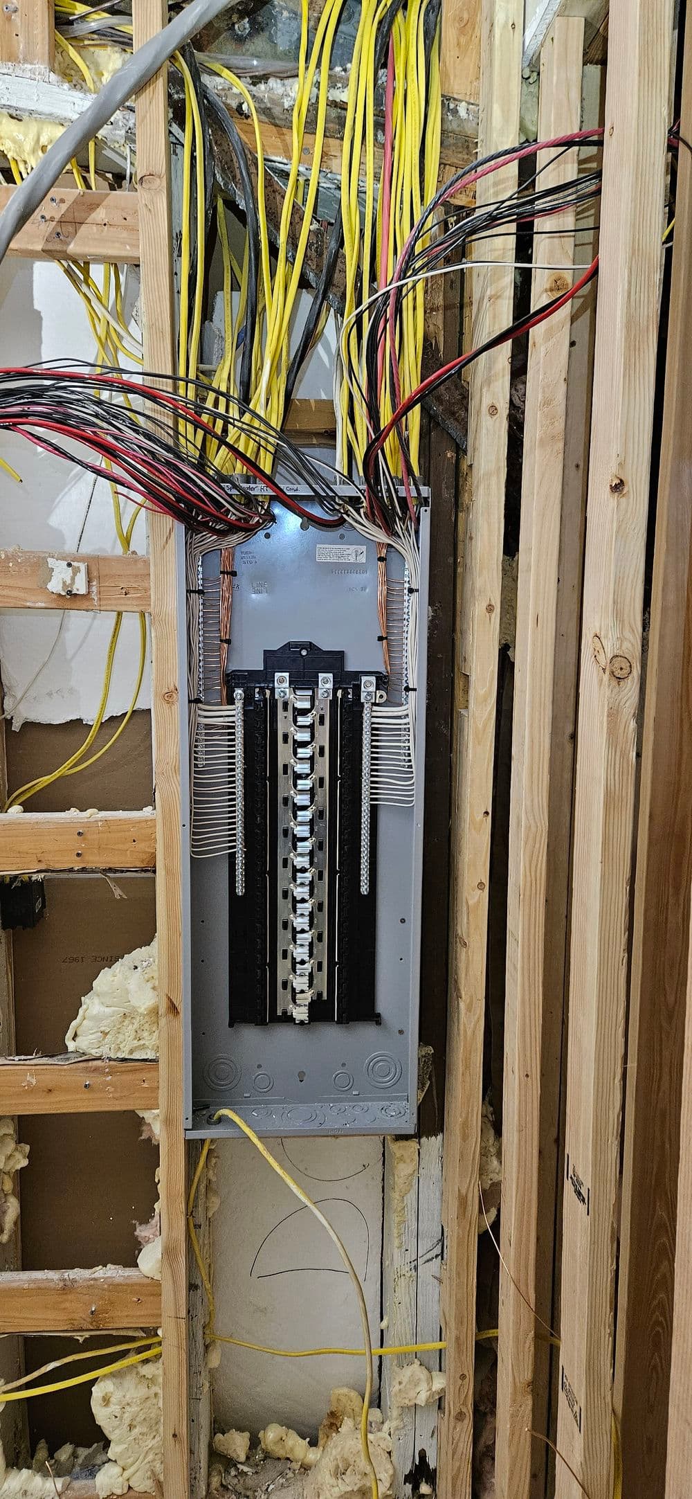 Electrical panel installation in a renovation, with exposed wires and framing visible.