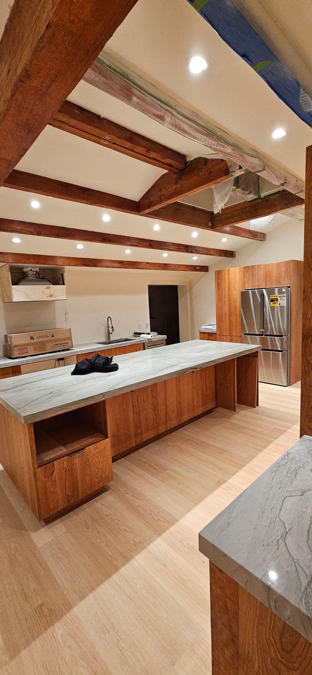 Modern kitchen featuring wooden beams, large island, and stainless steel appliances.